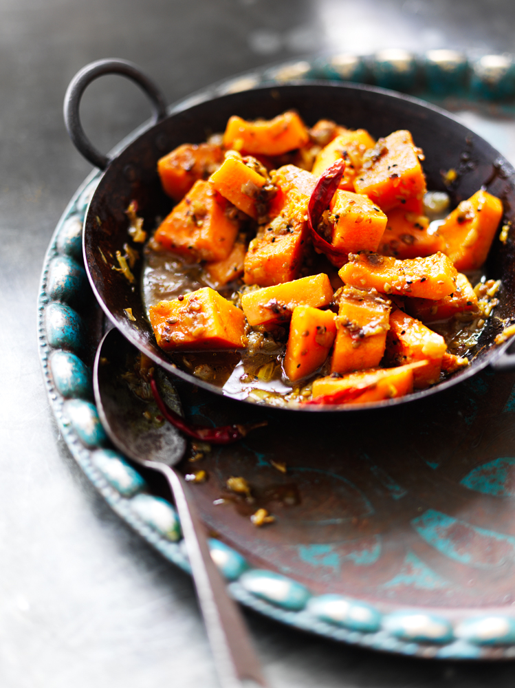 Photograph of a bowl of Bengali butternut squash curry with dried spices and a messy spoon
