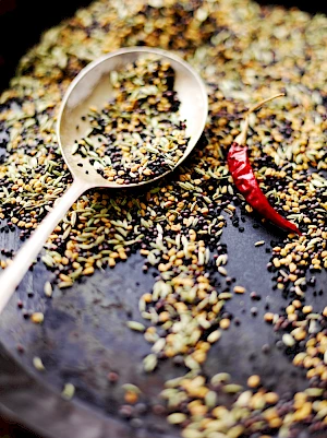 Photograph of dry spices being dry fried in a pan and a spoon with some of the spice mix