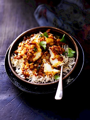 Photography of bowl of Chettinad Fish Curry with rice, garnished with coriander in a bowl with a fork