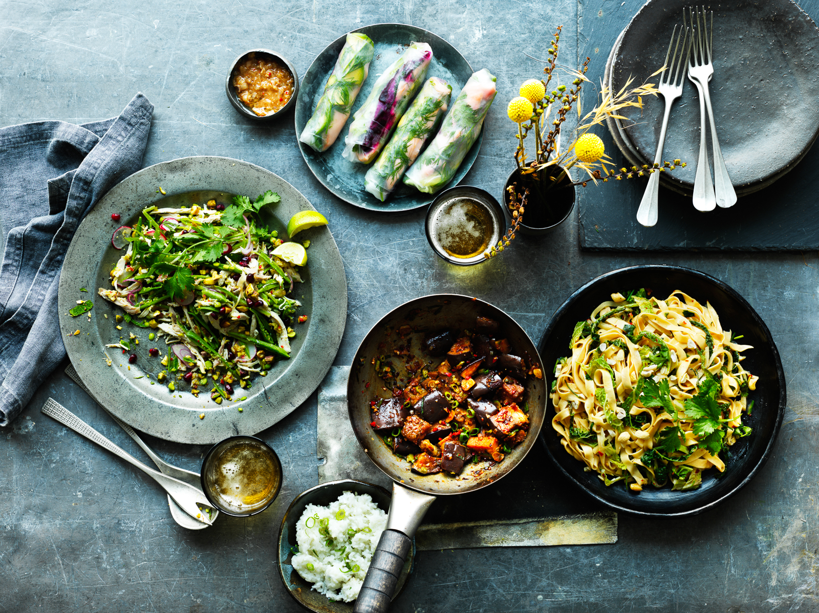 Photograph of a table top of dishes of Vietnamese food. Fresh spring rolls, aubergine curry, noodles. A feast.
