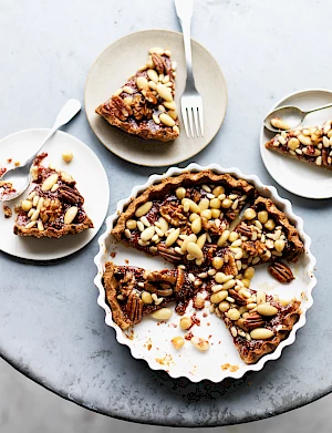 Photograph of almond crostata dessert in a pie dish with portions on plates with forks