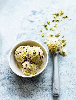 Photograph of pistachio ice-cream in a bowl and an ice-cream scoop with chopped pistachio nut