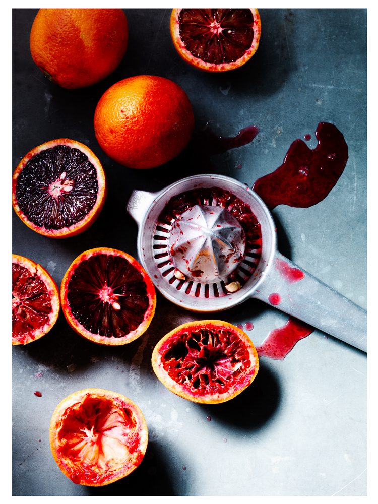 Photograph of blood oranges being juiced with metal hand juicer