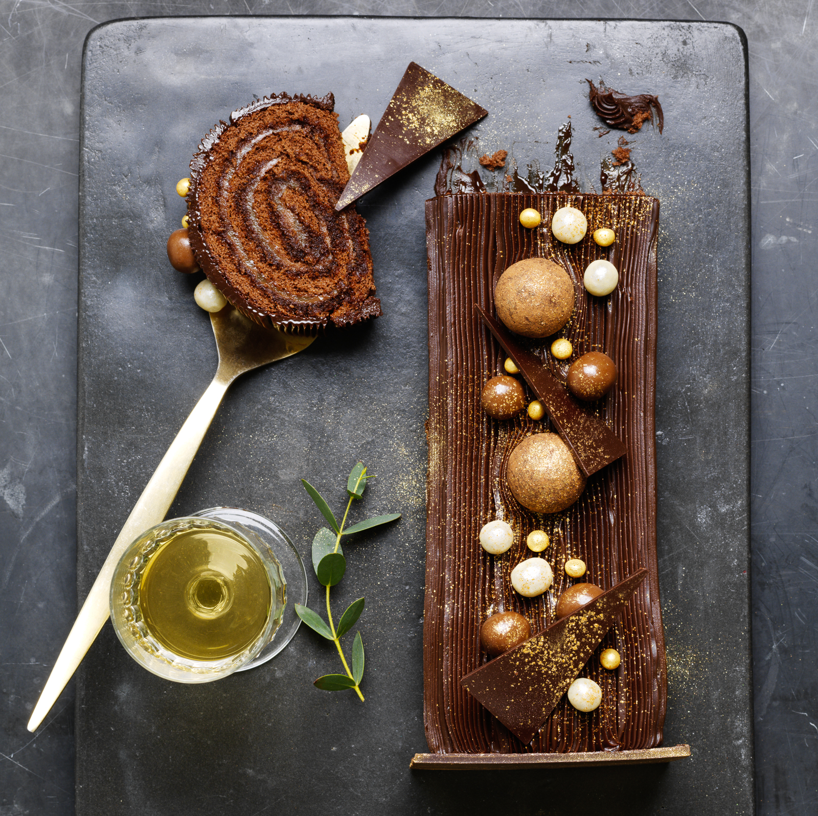 Photograph of Christmas chocolate log with chocolate balls of white, milk and dark chocolate with slice