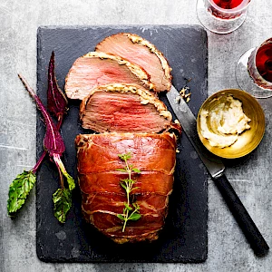 Photograph of roast beef joint stuffed with horseradish cream, carved slices and baby beetroot