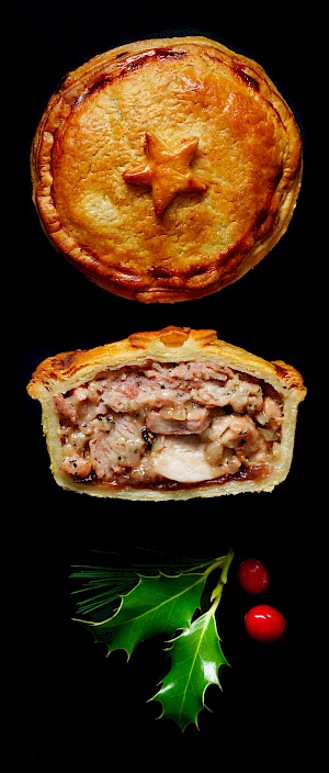 Photograph of a whole and half a festive turkey pie with holly and berries