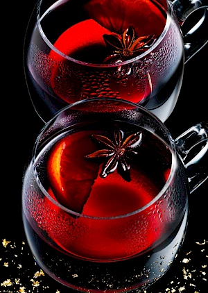 Photograph of glass cups of mulled wine with star anise and orange wedge