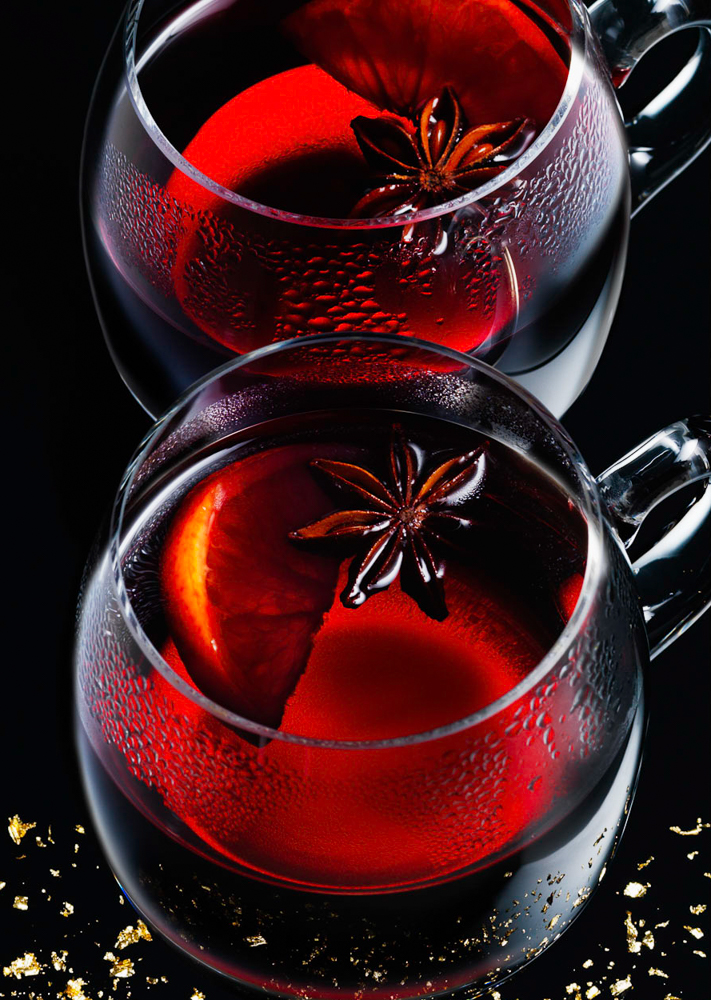 Photograph of glass cups of mulled wine with star anise and orange wedge